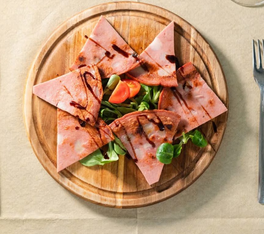Mortadella piastrata a triangoli con aceto balsamico su tagliere
